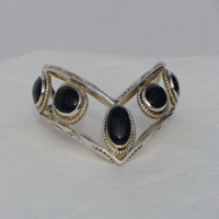 Five fouteen by ten millimeter oval Onyx stones bezel set connected by two triangular wires which are formed to a chevron shape. Worn with chevron pointing down